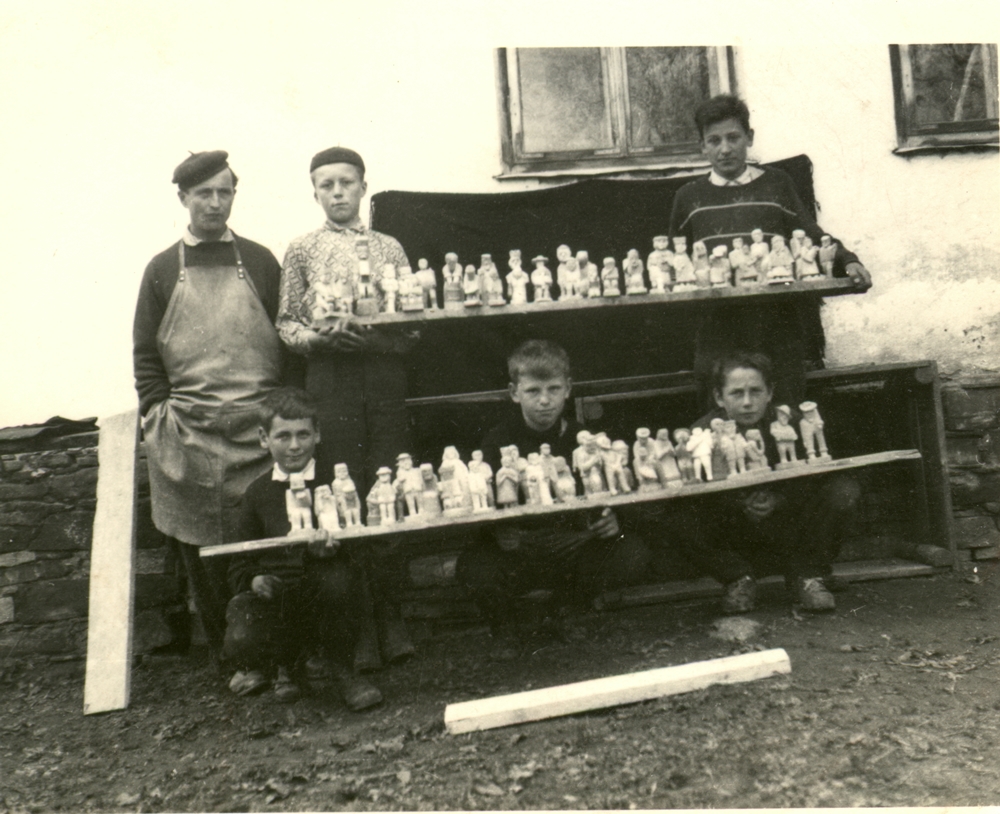 stare zdjęcie przedstawia dwie półki z rzeźbami, za którymi widać 5 dzieci i obok rzeźbiarza