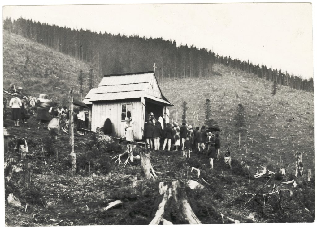 kapliczka na wykarczowanym stoku, wokół niej zgromadzeni ludzie w strojach góralskich