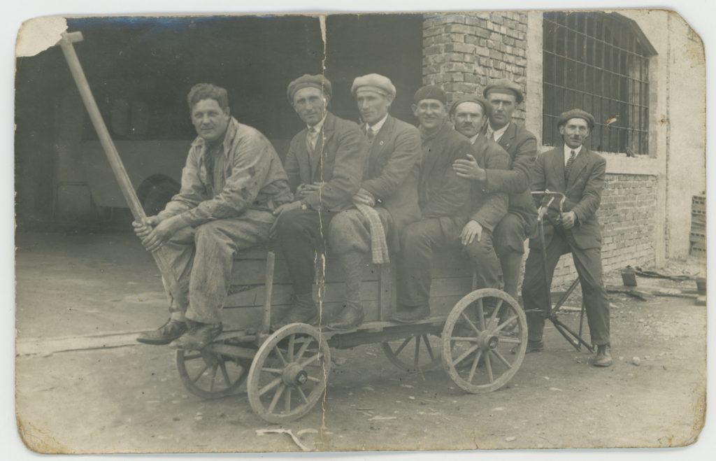 fotografia czarno-biała, grupa mężczyzn siedzący w drewaninym wózku