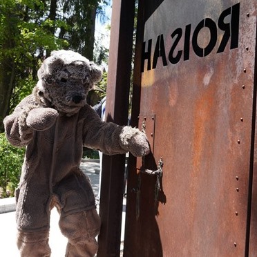 człowiek w stroju niedżwiedzia brunatnego stoi przy metalowych drzwiach z napisem Hasior