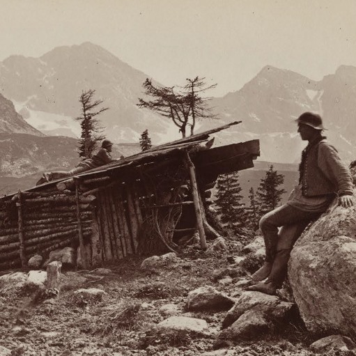 czarno białe zdjęcie. szałas pasterski , pasterz oparty o skałę na tyle panoramy Tatr