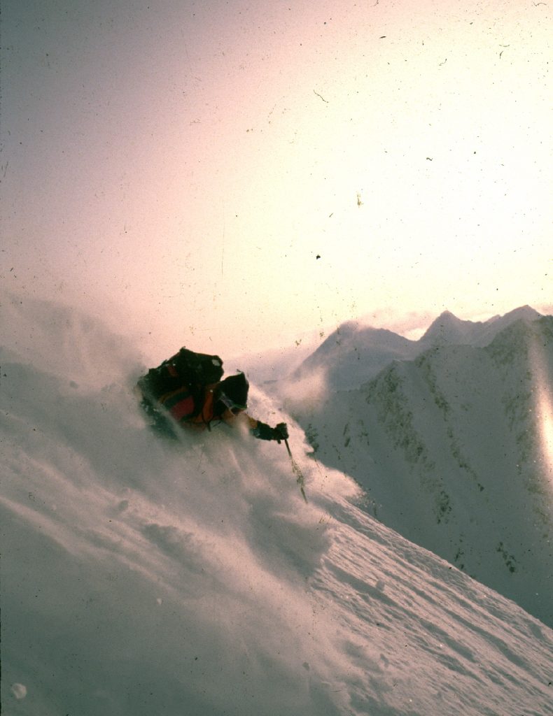 Fotografia przedstawia narciarza zjeżdżającego z ośnieżonego szczytu górskiego