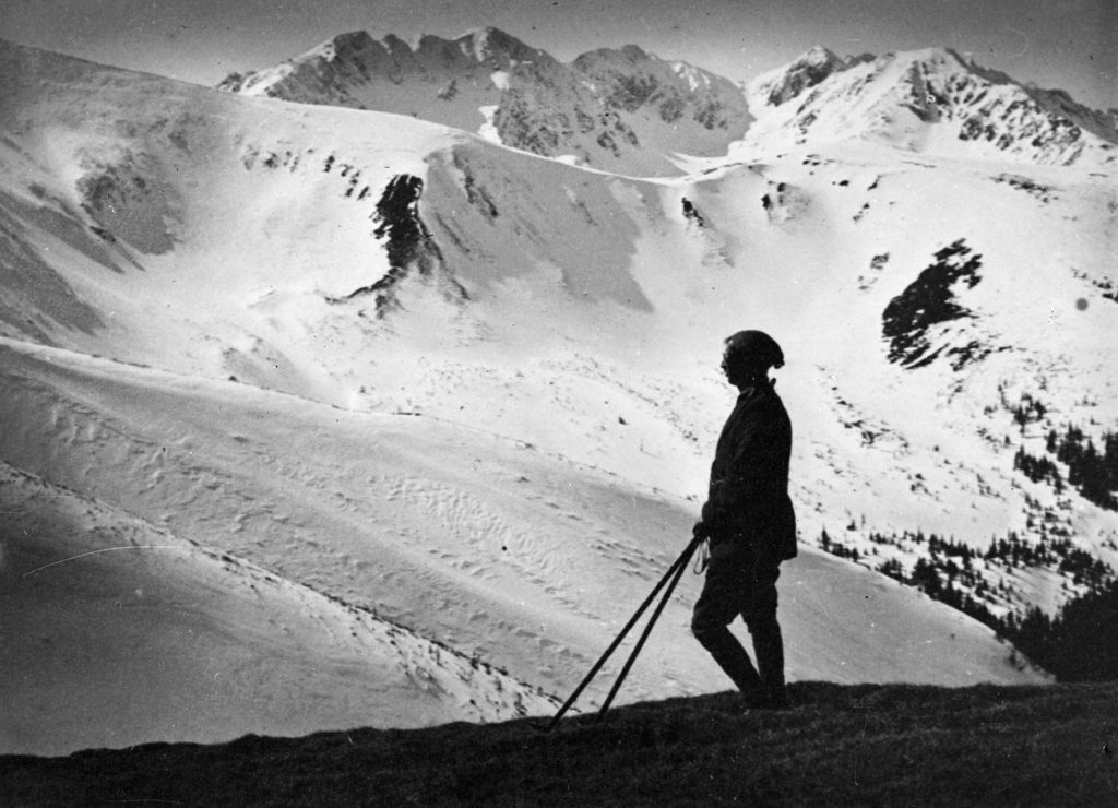 Czarno-biała fotografia, człowiek z kijkami na tle ośnieżonych gór