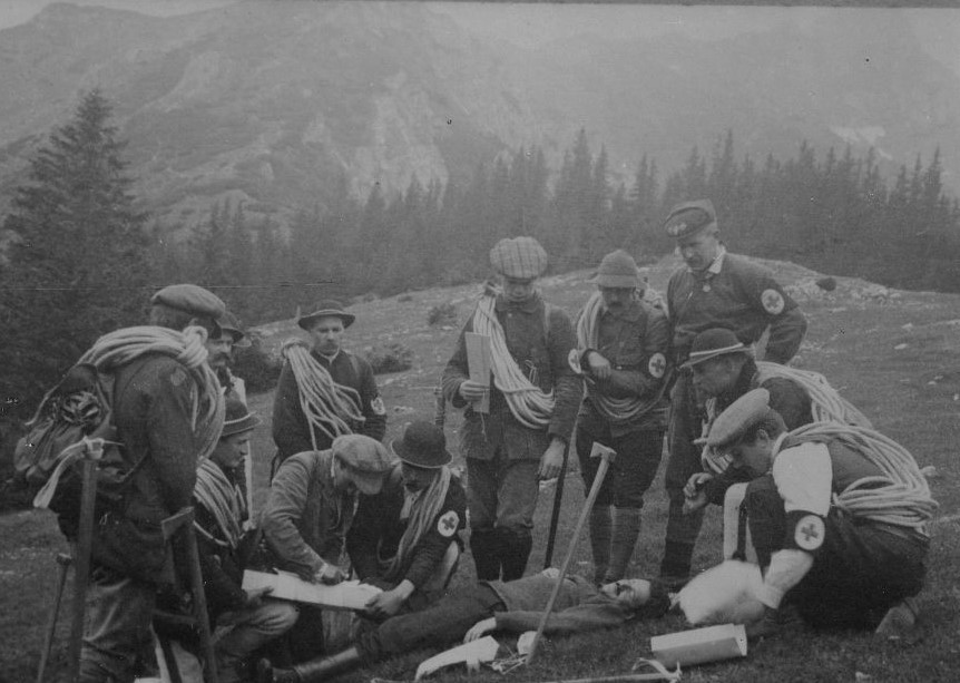 Czarno-biała fotografia Ćwiczenia TOPR z ratownictwa górskiego, najwyższy mężczyzna, stojący po prawej to Mariusz Zaruski, w tle widać Długi Giewont, fotokopia zdjęcia z prasy.