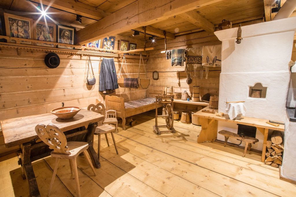 Wnętrze góralskiej chałupy, drewniane meble krzesła, skrzynia i półki i eksponaty wiszące na ścianach