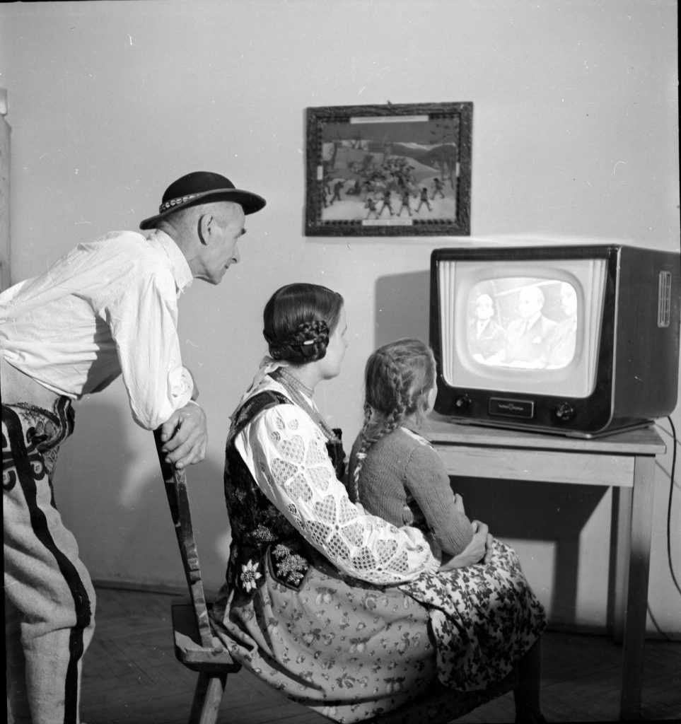 czarnobiałą fotografia - góralska rodzina oglądajaca pierwszy program w telewizorze.