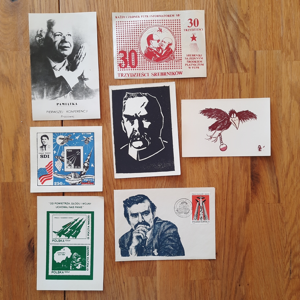 na drewnianym stole leży siedem znaczków o tematyce opozycyjnej z czasów PRL
