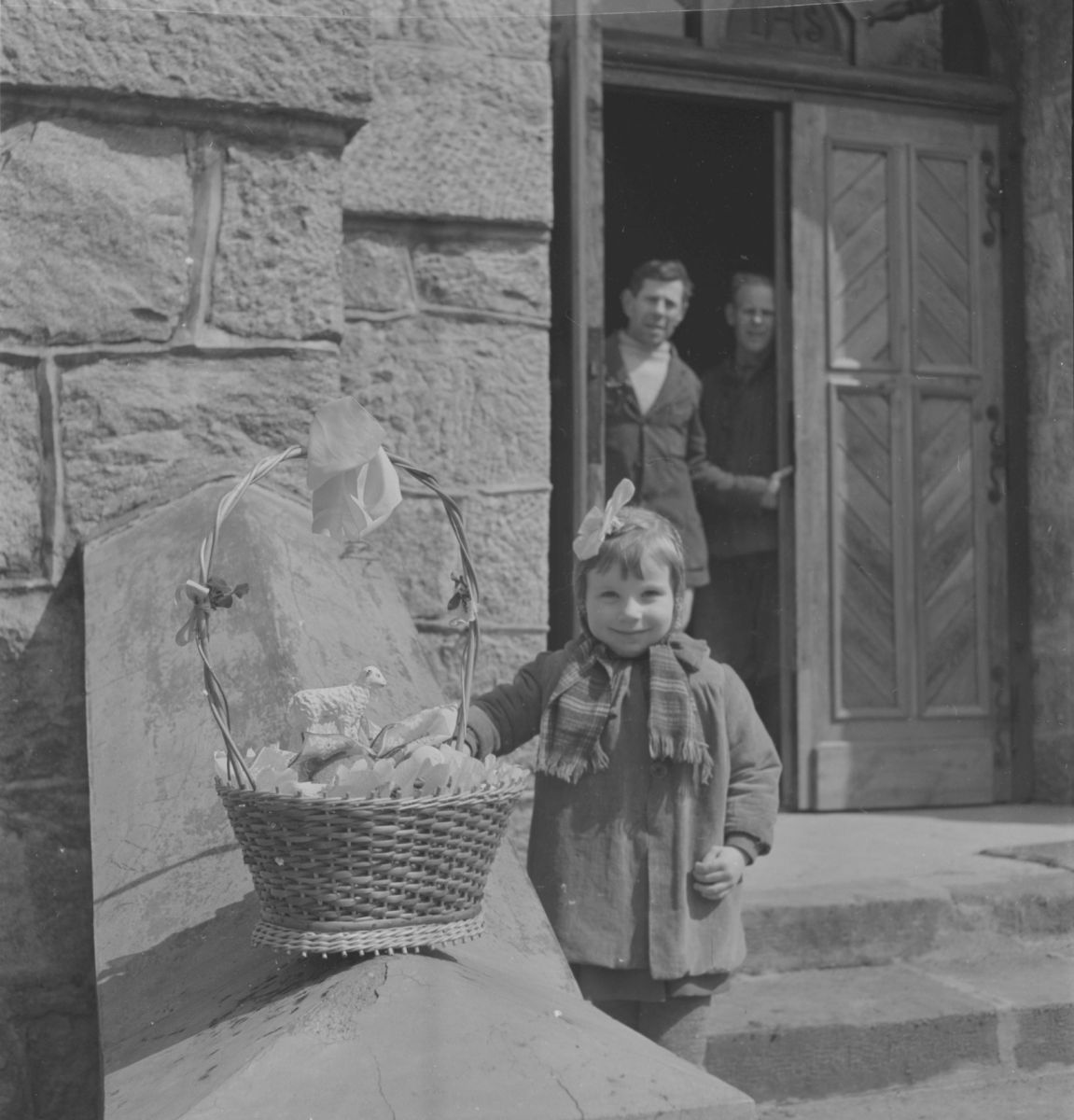 Wielkanoc w Białce Wielka Sobota. Dziewczynka stojąca przed wejściem do kościoła z koszyczkiem wypełnionym pokarmami wielkanocnymi zwanymi "święcelinami".