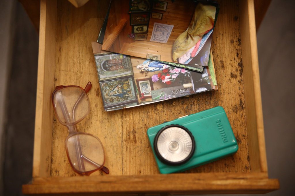 Na zdjęciu widzimy otwarta szufladę z okularami, starą latarką i fotografiami.