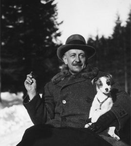 Zdjęcie przedstawia Kornela Makuszyńskiego trzymającego psa, z przodu dorysowano tort ze świeczką, z tyłu widać Giewont.