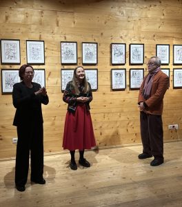 Na zdjęciu stoją trzy osoby - kuratorzy wystawy: Marek Krzysztof Lasecki i dr Emilia Pomiankiewicz-Wagner oraz tłumaczka języka migowego na tle rysunków prezentowanych na wystawie „SpotkajMY się w MT”.